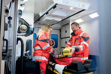 Ehrenamtliche Rettungskräfte der Johanniter arbeiten gemeinsam im Inneren eines Rettungswagens. Sie überprüfen die medizinischen Geräte und Taschen, um für einen Notfall gerüstet zu sein.