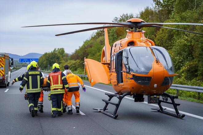 Rettungshubschrauber Christoph 4 steht auf der Autobahn zusammen mit Helfenden von der Feuerwehr und der Besatzung des Rettungshubschraubers.