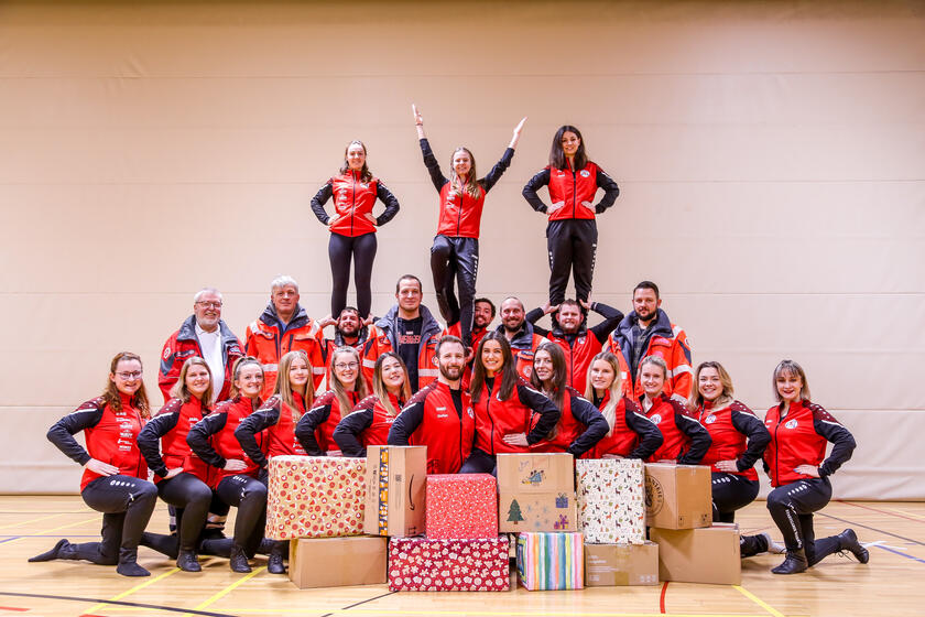 Mitglieder der Stadtgarde Wasserburg in einer Turnhalle, posierend mit Geschenkpaketen für den Johanniter-Weihnachtstrucker. Drei Personen stehen oben auf einer menschlichen Pyramide.