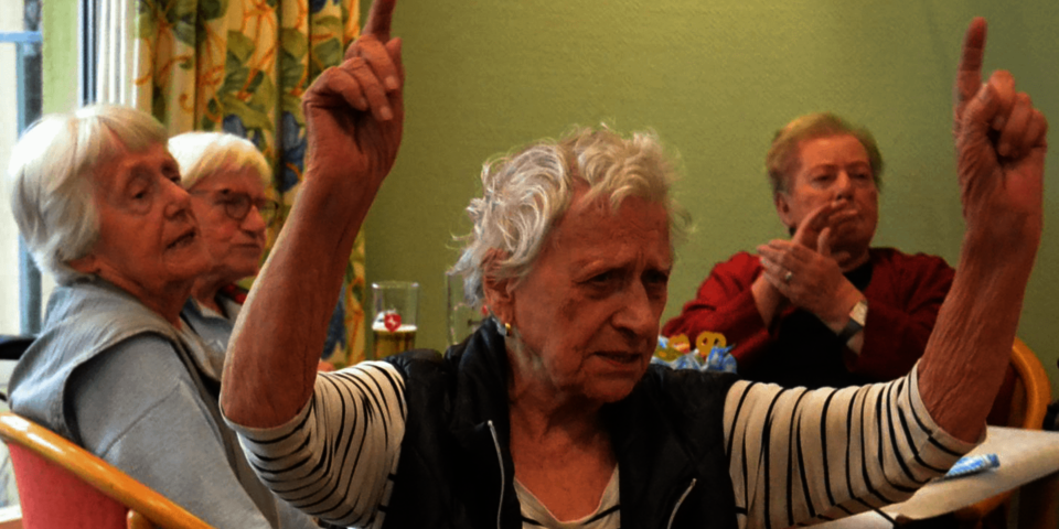 Eine ältere Frau hält beide Arme in die Luft, also ob sie dirigieren würde.