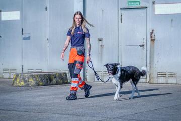 Einsatzkraft führt einen schwarz-weißen Hund an der Leine über einen Hof.