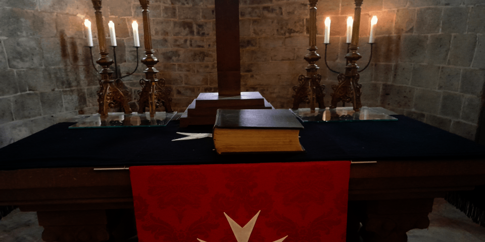 Altar mit brennenden Kerzen und einem Antependium mit Johanniter-Zeichen
