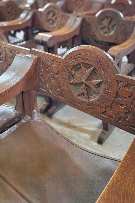 Ein alter Holzstuhl mit einem herausgeschnitztem Johanniter-Kreuz in einer Kirche.
