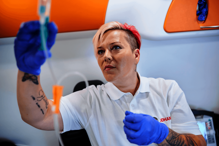 Arbeit mit kühlem Kopf und warmem Herz: Rettungsdienst bei den Johannitern Eine junge Frau bei ihrer Arbeit im Rettungswagen. Sie trägt blaue Handschuhe und ein weißes Polo mit Johanniter-Logo. Ihre Haare sind kurz geschnitten und bunt gefärbt.