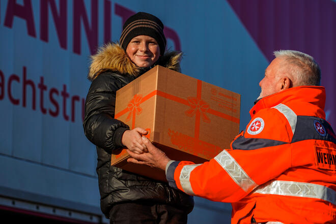 Das Bild zeigt einen Johanniter, der einem Kind ein Paket vom Weihnachtstrucker überreicht.