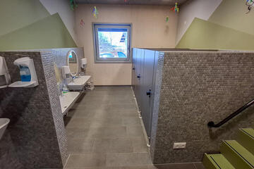 Kinderbad mit Waschbecken, Spiegeln und Toilettenkabinen, Fenster am Ende.