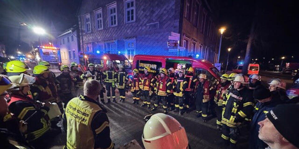 Einsatzkräfte in der Nacht in einer Altstadt. Im Hintergrund brennt ein Haus.