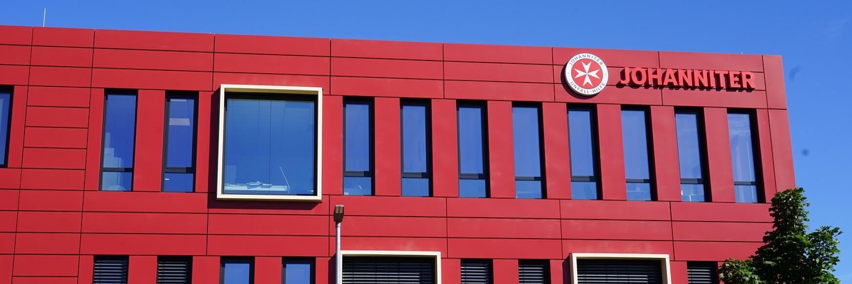 Man sieht ein großes, rotes Gebäude mit dem Schriftzug "Johanniter"
