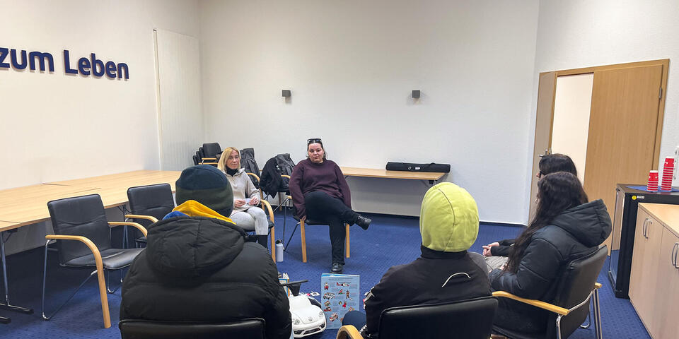 In einem großen Raum sitzen Schüler und hören zwei Frauen zu, die ebenfalls auf Stühlen sitzen