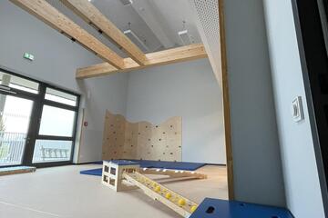 Ein Raum mit hoher Decke, verschiedenen Turn- und Bewegungsmöglichkeiten und einer kleinen Kletterwand.