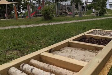 Ein sogenannter Barfußpfad auf der Wiese, das ist ein Weg aus verschiedenen Materialien wie Holz, Steinchen und Sand, über den man barfuß laufen kann. 