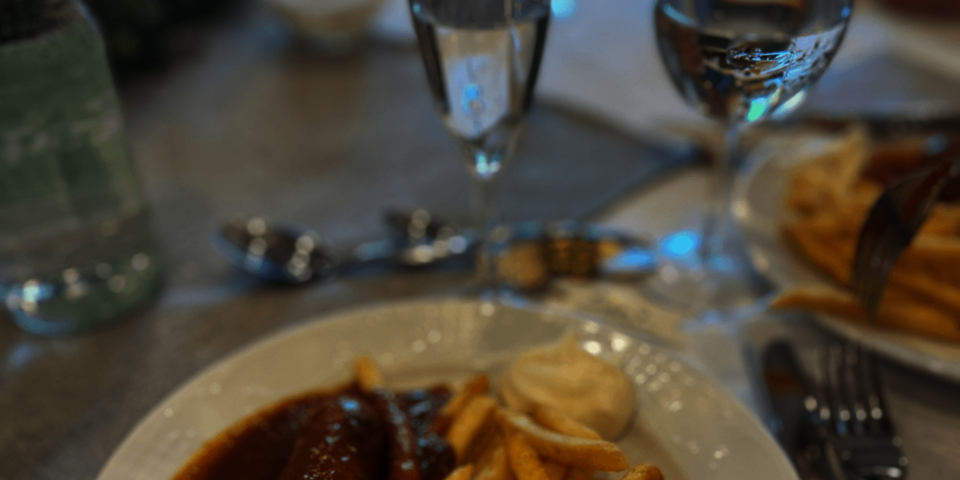 Blick auf einen gedeckten Tisch mkt Gläsern; ein Teil eines Tellers mit Pommes frites und Currywurst