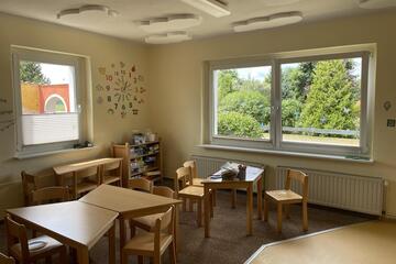 Innenbereich der Kita Pustewind, mit Tischen und Stühlen und großen Fenstern