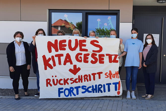 Mehrere Kitamitarbeiter halten ein Plakat hoch auf dem steht: Neues Kitagesetz ist Rückschritt statt Fortschritt
