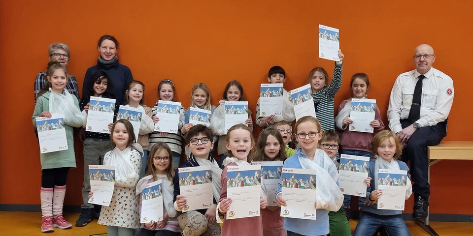 Sich freuende Kinder mit Zertifikaten, ein Johanniter und zwei Frauen
