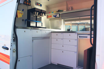 Der geöffnete Innenraum eines Transporters mit Blick auf die Theke, viele beschriftete Schränke und Vorräten sowie einer Kaffeemaschine.
