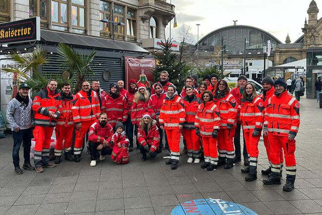 Eine große Gruppe mit Menschen in Johanniter-Uniform stehen zusammen. Im Hintergrund sieht man den Frankfurter Hauptbahnhof.