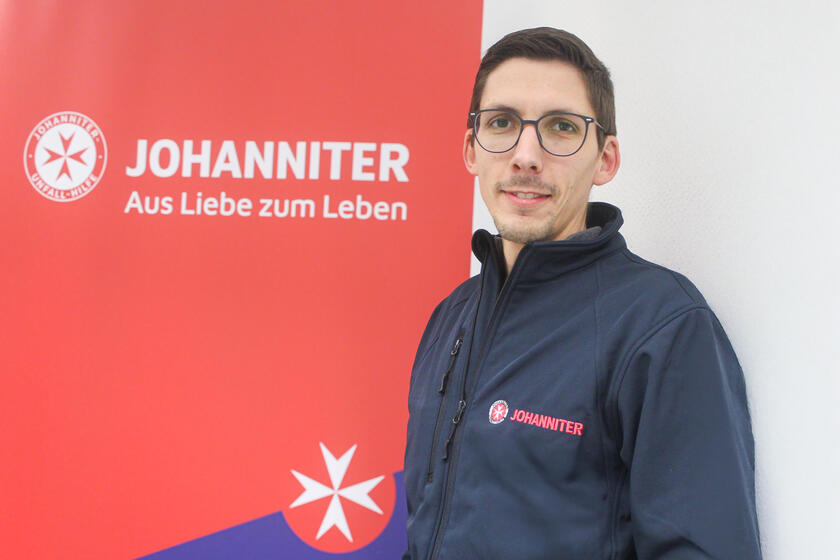 Ein Mann mit blauer Johanniter-Jacke vor einem Roll-Up mit Johanniter-Logo.