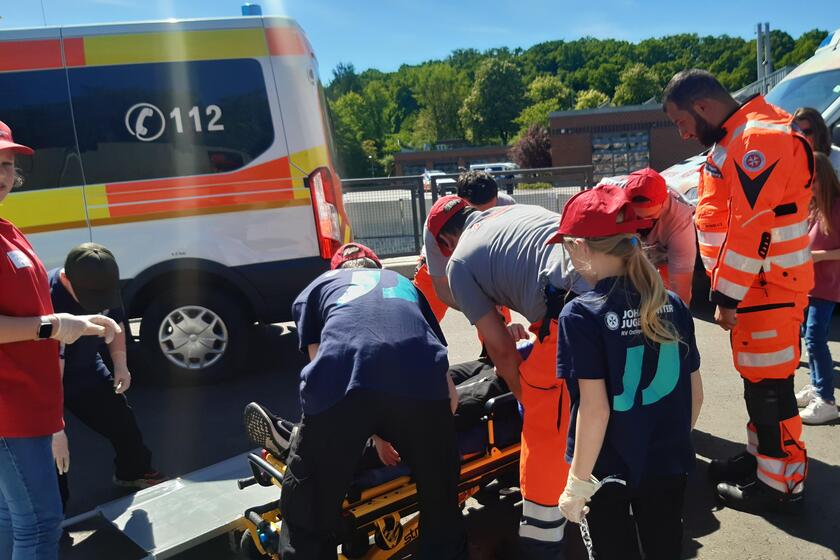 Jugendmitglieder und hauptamtliche Einsatzkräfte stehen um eine Trage und versorgen eine verletzte Person