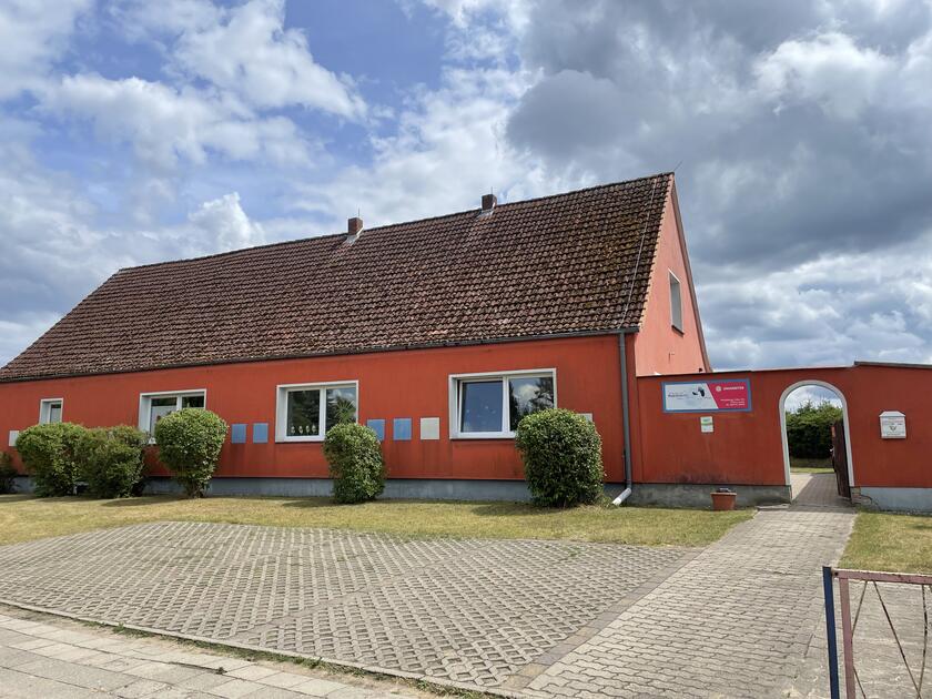 Ein orangenes Kita Gebäude, mit großen, weißen Fenstern und einer Tür, die zum Hof führt