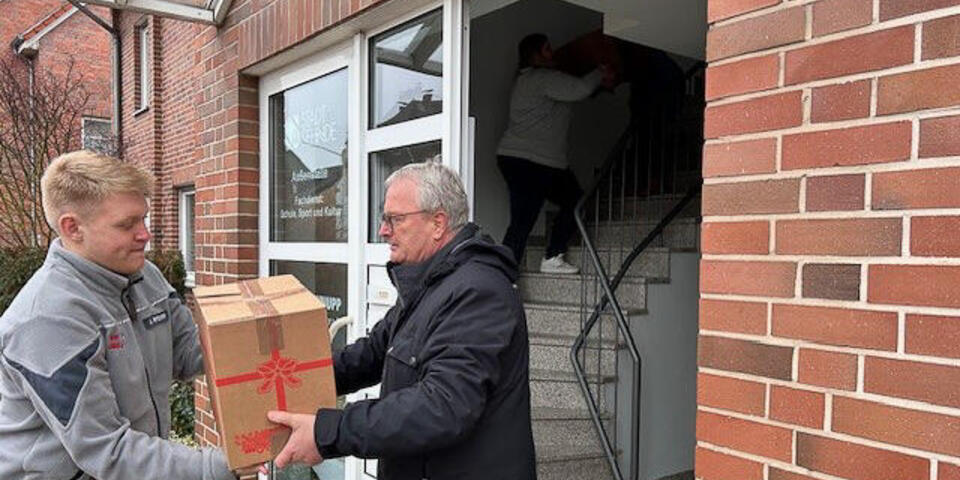 Ein Mann reicht aus einer Haustür einem jungen Johanniter ein Weihnachtstruckerpaket an