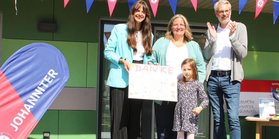 Zwei Frauen halten ein Schild hoch daneben ein kleines Mädchen und ein Mann 