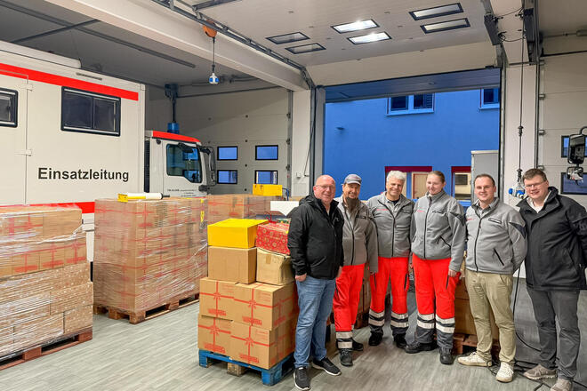 In der Fahrzeughalle stehen Paletten mit Paketen und sechs Helfer der Johanniter.