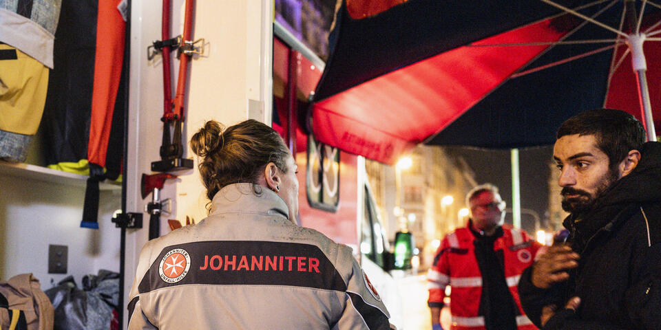 Ein Obdachloser steht vor einer Johanniterin beim Pflasterlaster.