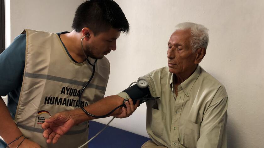 Ein Mitarbeitender unserer Partnerorganisation misst den Blutdruck eines älteren Herren