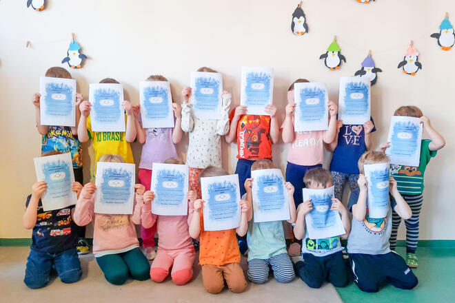 Die Kinder der Kita Gänseblümchen stehen für ein Gruppenfoto zusammen und halten sich die Urkunden vor das Gesicht.