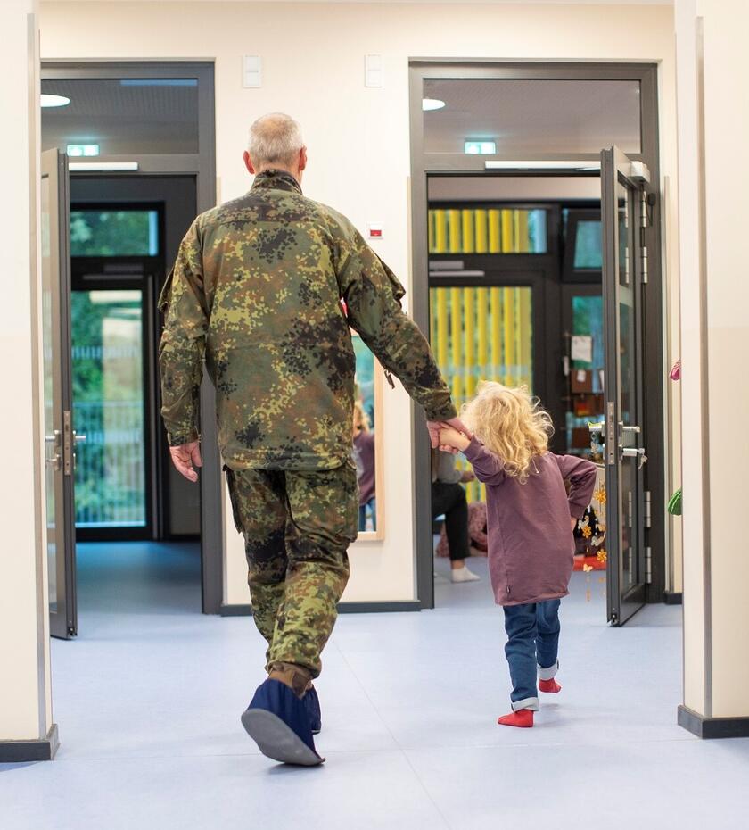 Ein Bundeswehrsoldat in Uniform bringt sein Kind an der Hand zur Kita.