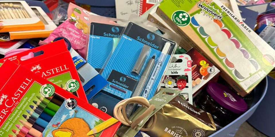 Ein blauer Korb prall gefüllt mit Schulartikeln, Speisen und Kosmetikartikeln für die Johanniter-Suppenküche.