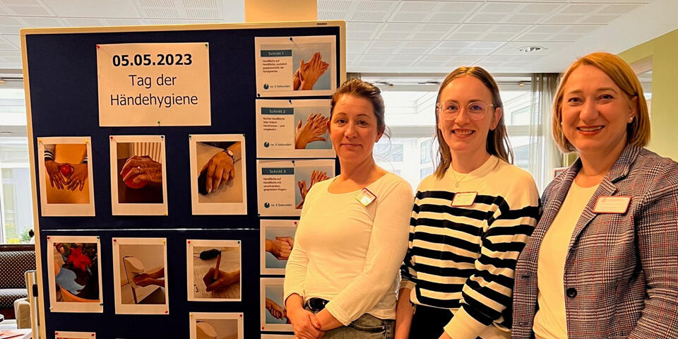 Drei Frauen stehen neben einer Stellwand mit Bildern.