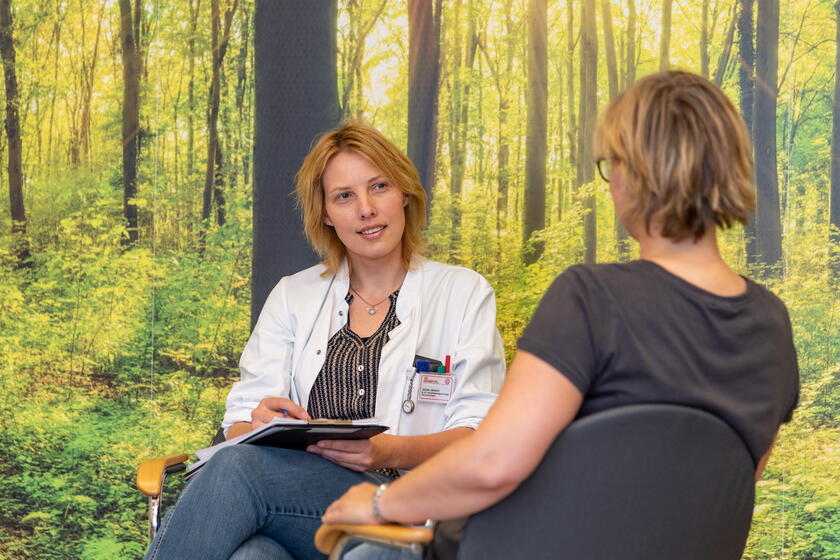 Ärztin bei einem Gespräch mit einer Patienten vor einer Waldtapete