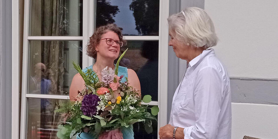 Eine Frau übereicht einer anderen Frau einen Blumenstrauß