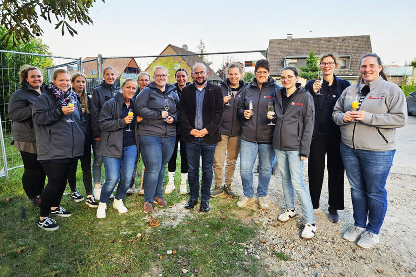 zwölf Johanniterinnen und Johanniter stehen mit einem Sektglas mit Orangensaft zusammen