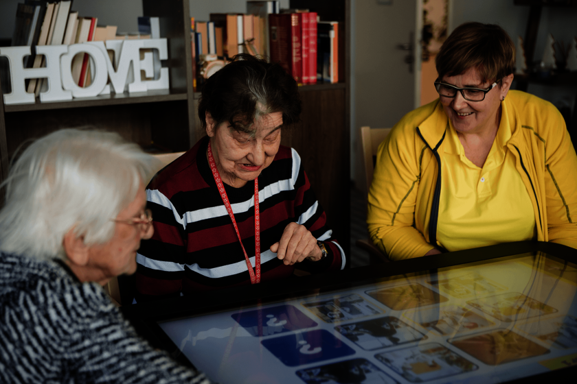Drei Seniorinnen spielen gemeinsam an einem digitalen Tisch.