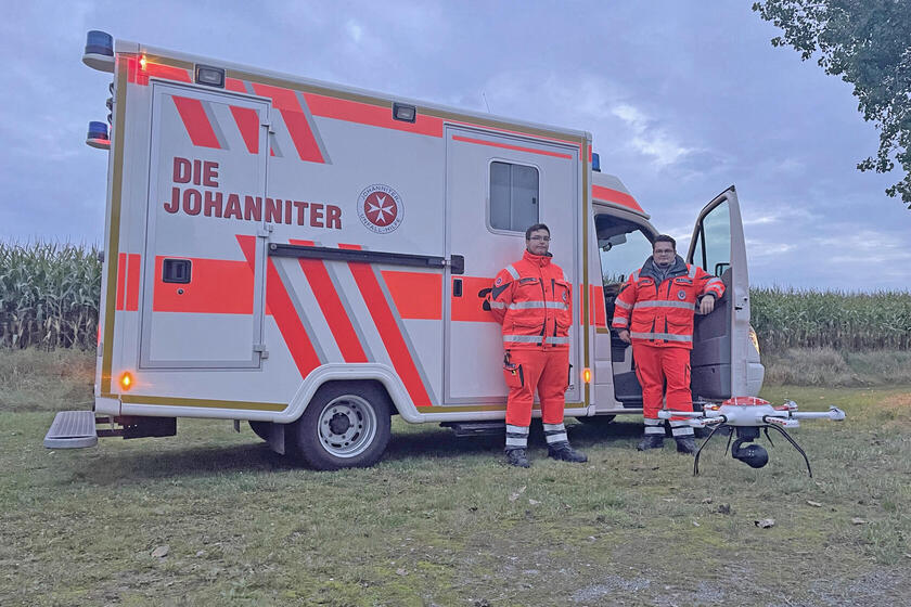 Zwei Einsatzkräfte vor einem Rettungswagen. Vor ihnen eine Drohne