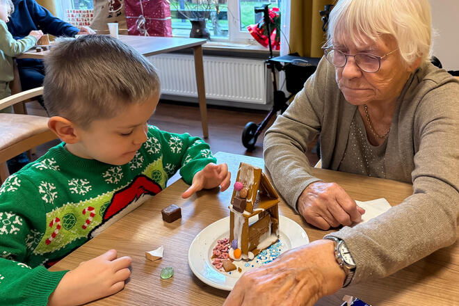 Generationsbrücke bei der Johanniter-Kita Kleine Hanseaten Ein Junge dekoriert gemeinsam mit einer älteren Frau ein Lebkuchenhaus.