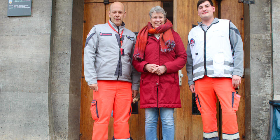 Ein Frau und zwei Johanniter vor einer Schule
