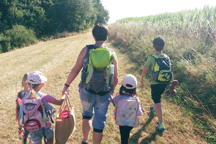 Vier Kinder und eine Frau gehen mit kleinen Rucksäcken am Rand eines Feld vorbei.