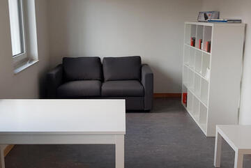 Gemütlicher Raum mit Sofa, Tischen und Regal.
