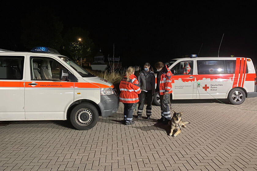 Einsatzteam steht gemeinsam mit Rettungshund von den Einsatzfahrzeugen und bespricht sich. 