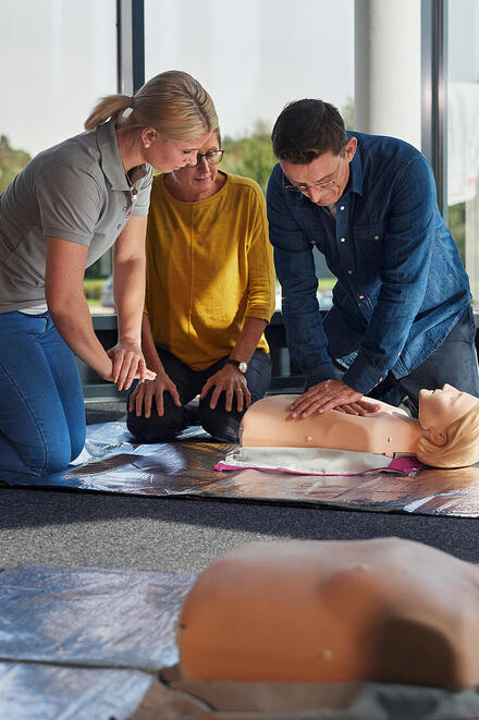 Eine Erste-Hilf-Kurs-Trainerin der Johanniter zeigt einem Mann die Herzdruckmassage an einer Übungspuppe.