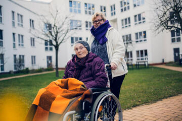 Bewohnerin im Rollstuhl wird von der Betreuerin im Garten des Johanniter-Quartier Lübeck spazieren gefahren
