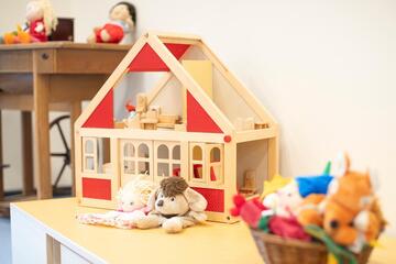 Ein Tisch mit einem Puppenspielhaus sowie Puppen und Kuscheltieren.