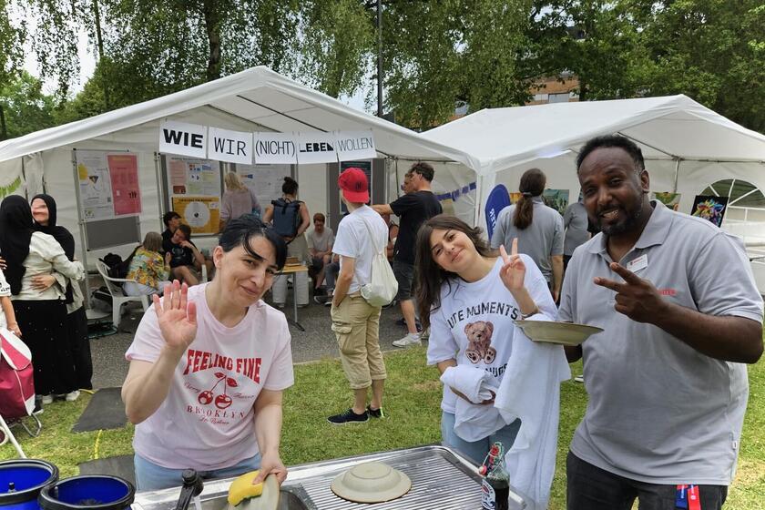 Drei Mithelfende posieren beim Abwasch für das Foto, im Hintergrund sind Zelte mit Teilnehmenden der Veranstaltung zu sehen.
