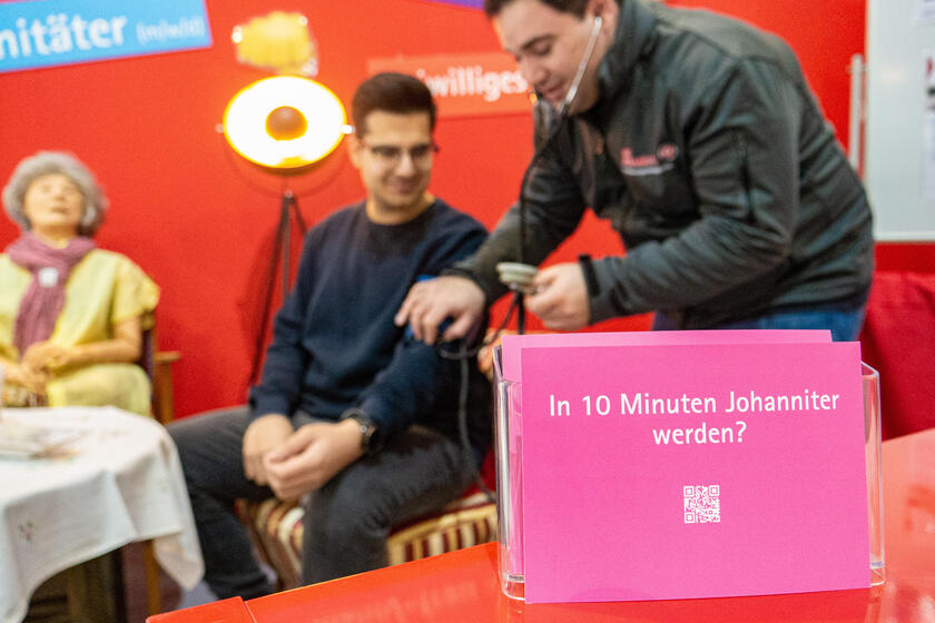 Am Messestand der Johanniter übt ein junger Mann das Blutdruckmessen.