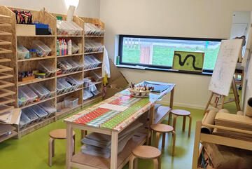 Basteltisch in der Mitte des Raum, umgeben von zahlreichen Regalen mit Materialien zum kreativ werden.