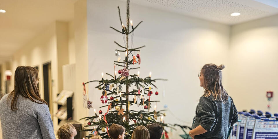 Kinder und zwei Frauen vor einem geschmückten Weihnachtsbaum in einem Krankenhaus